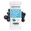 A single H3RO protein bar wrapper on a white background, surrounded by blueberries. The wrapper is white with a light blue label block detailing the ingredients: 3 egg whites, 12 blueberries, 5 almonds, 5 cashews, and 3 dates.